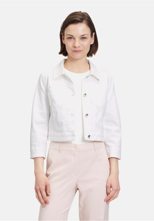 Giacca in denim bianco cropped con maniche lunghe, dotata di due tasche sul petto e chiusura con bottoni davanti. Indossata sopra una maglietta bianca e pantaloni rosa chiaro.