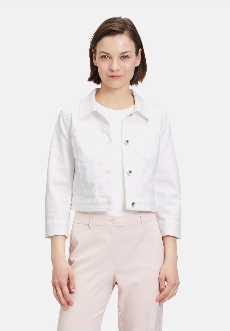 Weiße Denim-Cropped-Jacke mit langen Ärmeln, zwei Brusttaschen und vorderem Knopfverschluss. Trägt sie über einem weißen Oberteil und hellrosa Hose.