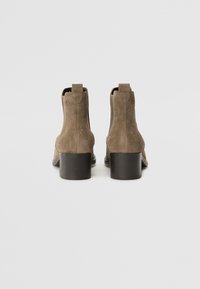 Bottes en daim marron, à cheville, avec un bout arrondi lisse et un petit talon carré. Dispose d'une languette à l'arrière pour un enfilage facile.
