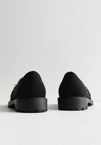 Black suede shoes with rounded backs, low black soles, and a subtle metallic accent. Textured surface and streamlined design.