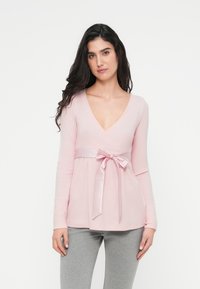 Top de manga larga de color rosa claro con escote en V y cintura plisada decorada con una cinta de satén anudada en un lazo. Textura acanalada suave, ajuste holgado.