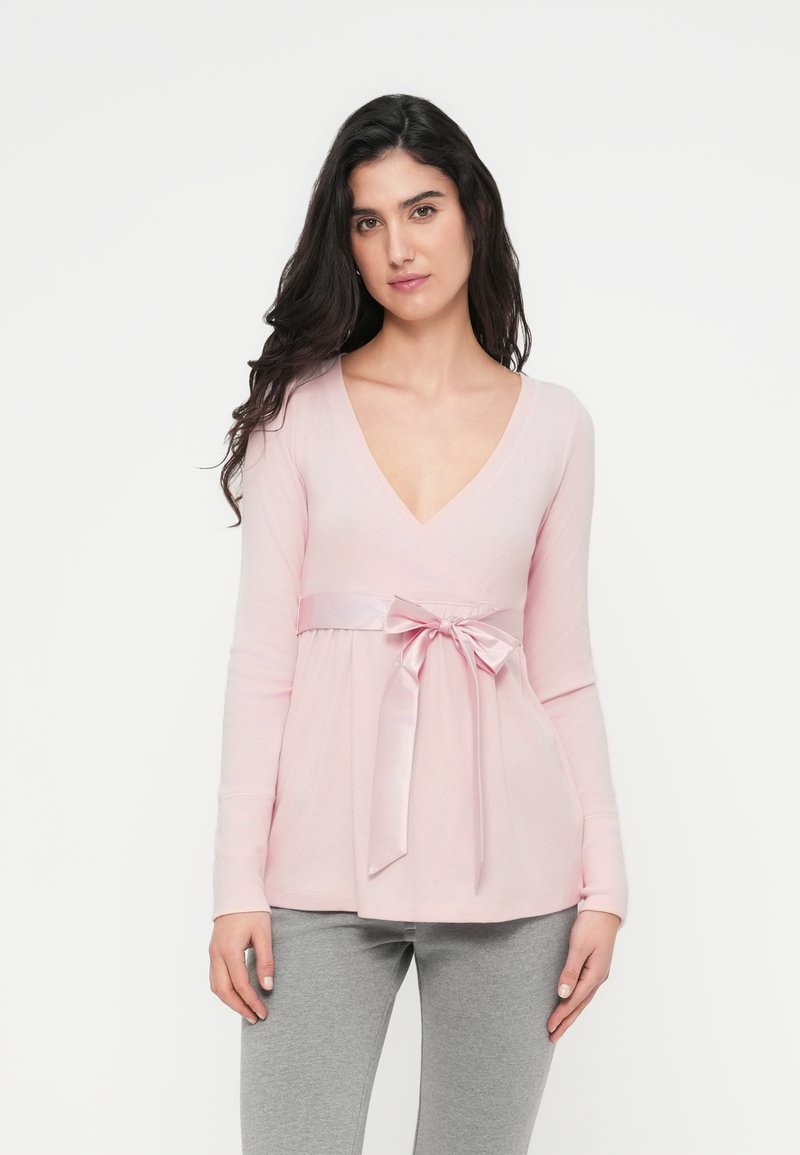 Top de manga larga de color rosa claro con escote en V y cintura plisada decorada con una cinta de satén anudada en un lazo. Textura acanalada suave, ajuste holgado.