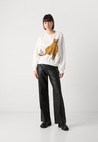 Felpa bianca con design a stampa leopardata e macchie arancioni, con la scritta "Jolly's Laundry". Abbinata a pantaloni in pelle neri a campana.