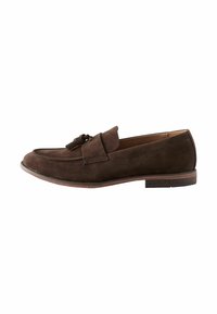 Mocasines de ante marrón con una correa decorativa y detalle de borlas, punta redondeada y un tacón bajo y apilado. Textura suave y diseño sencillo.