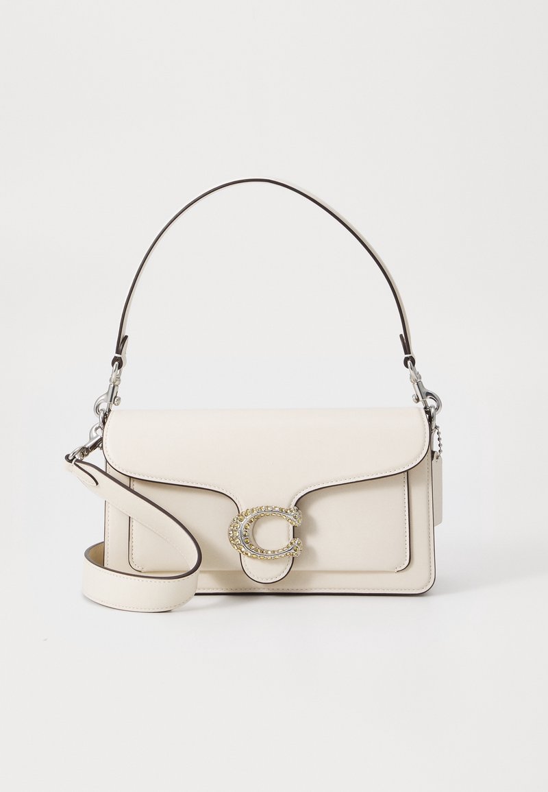 Sac à main en cuir couleur crème avec un fermoir orné d'or, une poignée courte et une bandoulière réglable sur fond blanc.