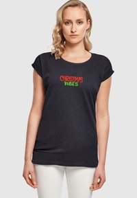 Sort T-shirt med korte ærmer, der har teksten "CHRISTMAS VIBES" i rød og grøn, med en afslappet pasform og rund Halsudskæring.