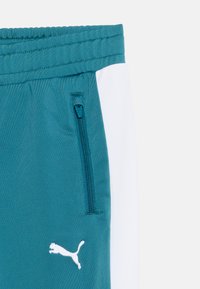 Τιρκουάζ αθλητικό παντελόνι με λευκή πλευρική ρίγα, ελαστική ζώνη μέσης, κάθετρη τσέπη με φερμουάρ και κεντημένο λευκό λογότυπο Puma.