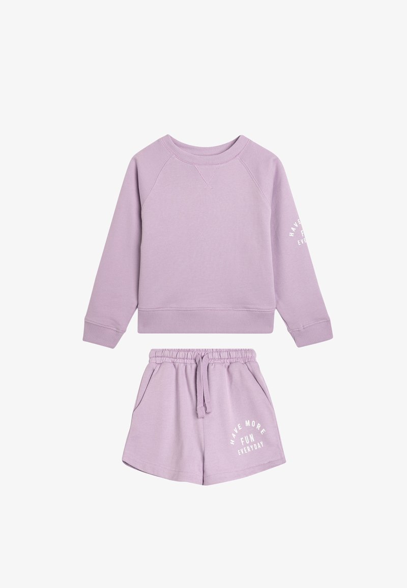 Il set di abbigliamento da loungewear in lilla comprende una felpa a girocollo con polsini a costine e pantaloni corti abbinati con coulisse. I pantaloni corti presentano un dettaglio di testo bianco.