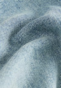 Svijetloplava denim tkanina s tkanjem u dijagonalnom uzorku, s mekim teksturama i suptilnim varijacijama boje. Vidljivo detaljno šivanje.
