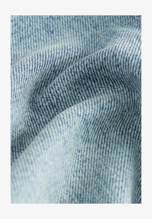Light blue denim fabric with a twill weave, featuring a soft texture and subtle variations in color. Detailed stitching visible.