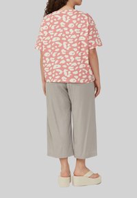 Rosa T-Shirt mit kurzen Ärmeln und weißen Leopardenflecken, kombiniert mit grauen weit geschnittenen Hosen. Das Modell trägt helle Plateausandalen.