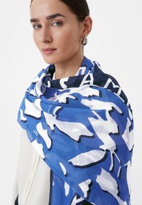 Niebiesko-biały szalik w wzory z abstrakcyjnymi kształtami, wykonany z lekkiej tkaniny, zarzucony na ramiona, o gładkiej fakturze.