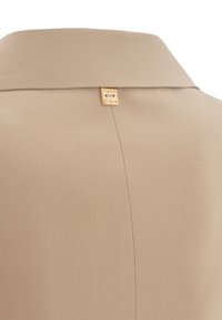 Indumento beige con collo a camicia; presenta un piccolo tag dorato "Manila Grace" sul retro, texture morbida e vestibilità sartoriale.