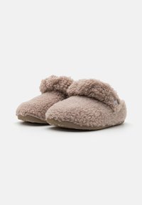 Ludna, fluffiga tofflor i en mjuk beige färg. Har ett brett band över toppen, med en texturerad innersula och en platt sula.