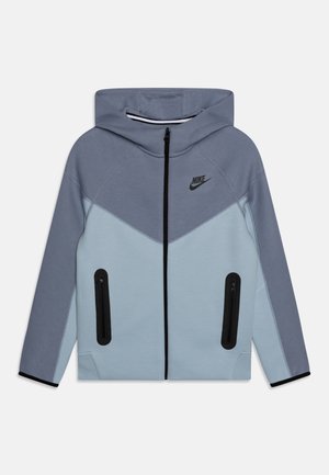 Hættetrøje fra Nike med lyseblå og grå paneler, sort lynlås i midten, lynlåslommer og Nike-logo på brystet.