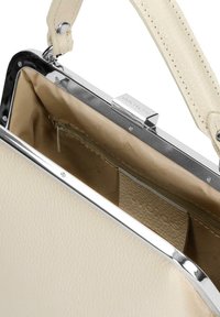 Kremowa torebka z sztucznej skóry z błyszczącą, srebrną metalową ramą. Wnętrze ma beżową podszewkę i zamykaną na zamek kieszeń do przechowywania.