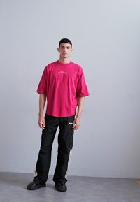 Rød oversized t-shirt med teksten "du er her", sorte cargo bukser med sidelommer og sorte platform sko. Enkel design, afslappet pasform.