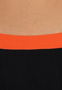 Svarta underkläder med ett orange elastiskt midjeband med präglad logotyp. Texturen är slät, med en åtsittande passform och inga synliga mönster.