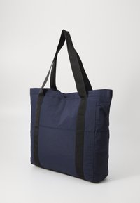 Marineblauwe stoffen draagtas met zwarte handvatten, rechthoekige vorm, gladde textuur en een drukknoopsluiting aan de bovenkant.