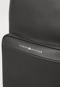 Schwarzer Rucksack aus glattem Kunstleder und strukturiertem Stoff, mit einem dezenten silbernen Logo auf der vorderen Tasche.
