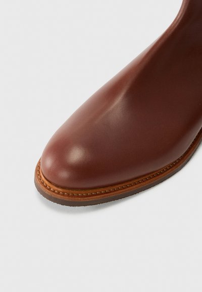 Pruun nahast ankle saapad ümmarguse varbaga, saleda siluetiga ja kontrastsete õmblustega talla äärtes detailideks. Sujuv tekstuur.
