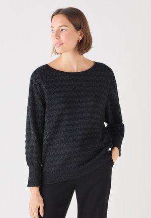 Pull en maille noire avec un motif texturé, décolleté bateau large et poignets côtelés. Associé à un pantalon noir pour un look harmonieux.