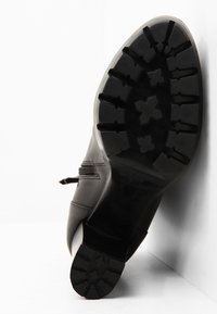 Černá kožená bota s robustní gumovou podrážkou s výrazným vzorem. Obsahuje boční zip pro snadné obutí a hladký povrch.