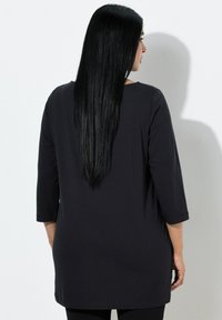 Černá tunika se tříčtvrtečními rukávy, měkká na dotek a volného střihu, sahající do poloviny stehen. Jednoduchý design bez vzorů a ozdob.