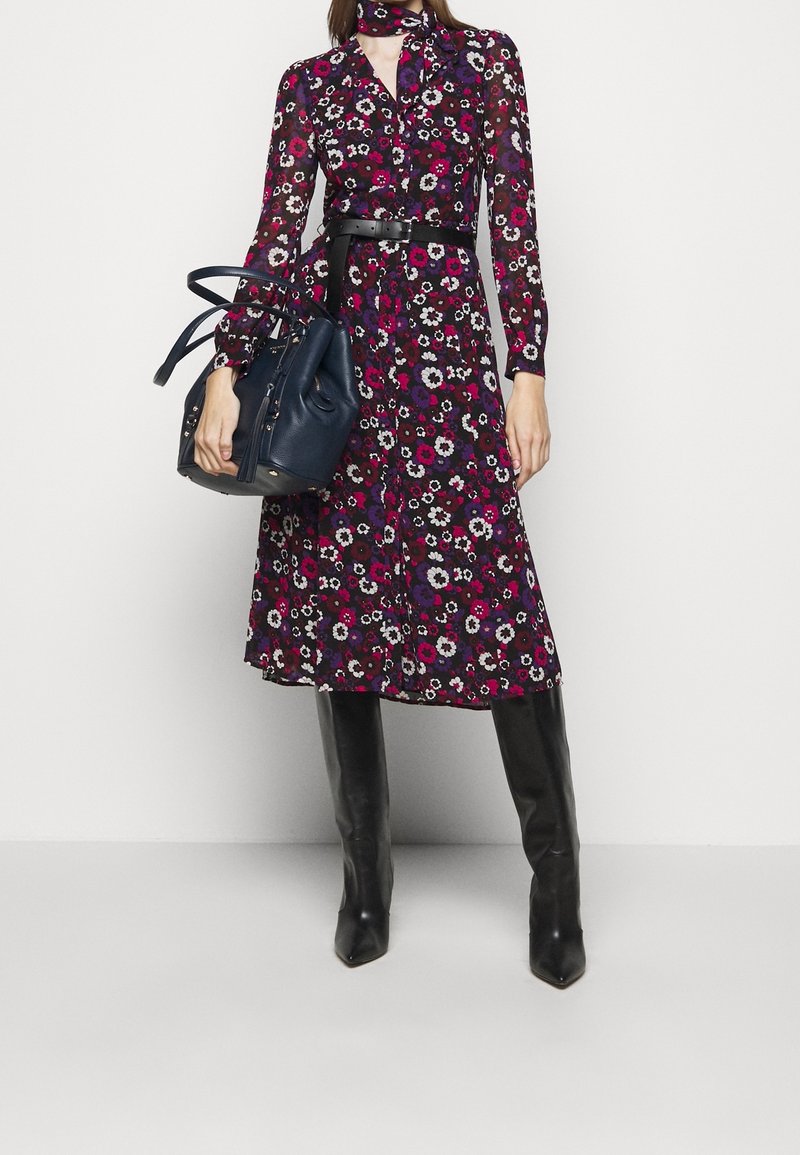 Květinové šaty v tmavě fialové a burgundské barvě, s dlouhými rukávy, páskem v oblasti pasu a sukní do kolen. Doplněny námořnickou kabelkou.