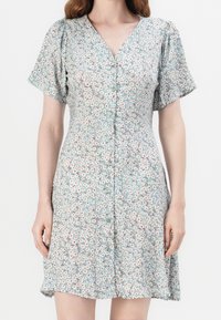 Robe florale vert clair avec des manches courtes bouffantes, décolleté en V et boutons sur le devant. Présente un motif de petites fleurs orange et blanches.