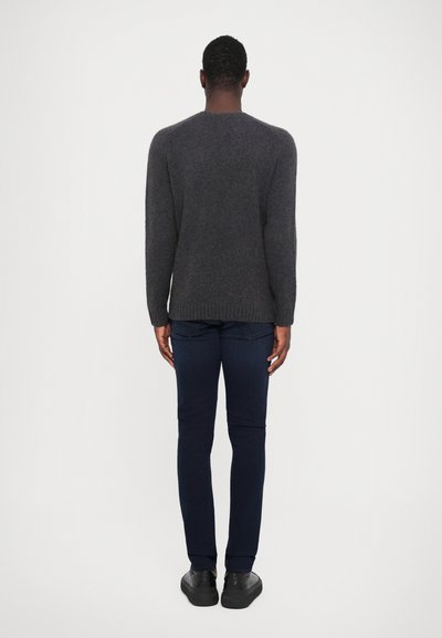 Grijze gebreide trui met een ronde hals, gecombineerd met donkerblauwe jeans. De trui heeft een geribde onderrand en lange mouwen. Zwarte schoenen maken de look compleet.