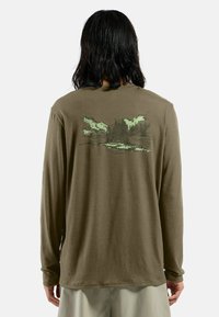 Langarmhemd aus gedämpftem olivgrünen Baumwollstoff mit einem Grafikdesign von Bergen und Wolken in hellgrün auf der Rückseite, im lässigen Schnitt.