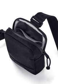 Borsa a tracolla nera in tessuto con chiusura a zip, foderatura interna grigia, tracolla regolabile e una patch con logo sul davanti. Design compatto e rettangolare.
