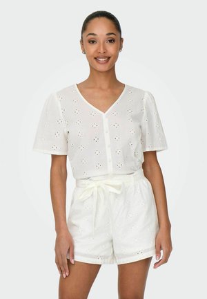 Haut en eyelet blanc avec des manches courtes et un décolleté en V, associé à un short blanc avec une taille à cordon. Les deux présentent des découpes à motifs.