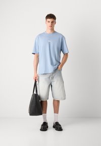 Ljusblå T-shirt, lös passform denimshorts, svart tote-väska, svarta loafers, vita strumpor. Minimalistisk design med avslappnad passform och neutrala färger.