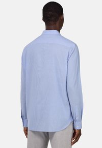 Camicia a righe azzurro chiaro, maniche lunghe, polsini con bottoni, orlo curvo, realizzata in tessuto morbido. Cuciture visibili e colletto standard.