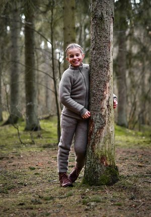 Trening gri din fleece cu bluză cu fermoar și mâneci elastice, combinat cu cizme maro cu șireturi, fată sprijinită de un copac într-o pădure.