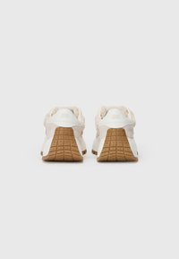 Adidași albi cu un panou de țesătură texturată, de culoare crem, la călcâi. Talpa este de culoare caramel, cu un design de profil structurat.