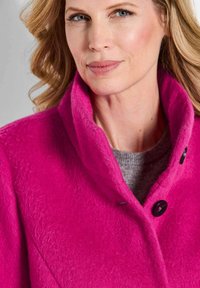 Fuchsia Wolle-Mantel mit hohem Kragen, der schwarze Knopfakzente aufweist. Weiche Textur und strukturiertes Design, das im Bild hervorgehoben wird.