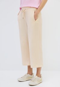 Beige, textured wide-leg pants with drawstring waist and side pockets, paired with light-colored sneakers.