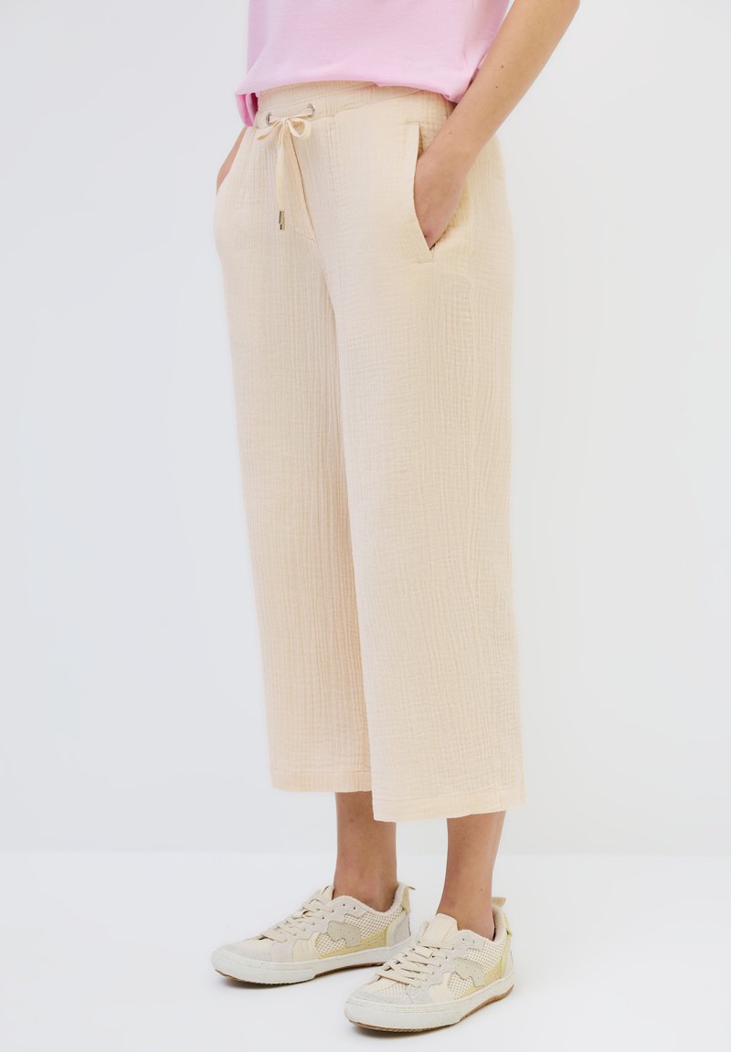 Beige, textured wide-leg pants with drawstring waist and side pockets, paired with light-colored sneakers.