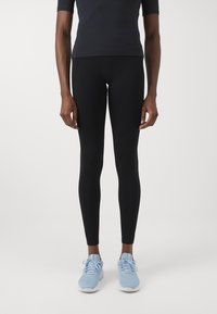 Schwarze Leggings aus dehnbarem Material, taillierte Passform, nahtlose Konstruktion, kombiniert mit hellblauen Sportschuhen.
