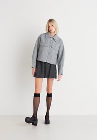 Besklippt grå zip-jacka med två framfickor, kombinerad med en svart randig kjol och knähöga svarta strumpor, bärs med klumpiga platåskor.