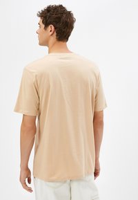 Beżowy t-shirt z krótkim rękawem wykonany z miękkiej bawełny. Posiada okrągły dekolt i luźny krój. Minimalistyczny design bez widocznych wzorów lub akcentów.