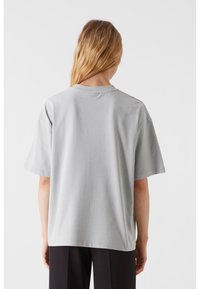 Világosszürke, oversize póló rövid ujjakkal, kerek nyakkal és puha pamut textúrával. A varrások minimalista kialakításúak, nincs látható grafika.