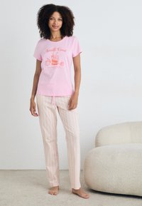 T-shirt de algodão rosa com gráfico "Costa Amalfitana", combinada com calças de pijama listradas em rosa claro e creme. Textura suave, ajuste casual.
