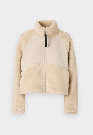 Beige fleecetrøje med høj krave, lynlås og raglanærmer. Designet med to frontlomme med lynlås og en cropped silhuet.
