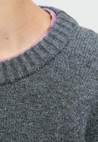 Sivi pleteni pulover z rebrastim ovratnikom, ki ima vijolično notranjost. Tekstura se zdi mehka in gosta, izdelana iz volne ali podobnega materiala.