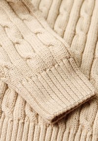 Beige gebreide trui met kabel- en geribbelde structuren, met een mix van gedraaide en verticale patronen in zachte garen.