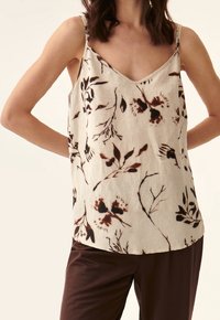 Beige tanktop met bloemenprint in bruin, dunne schouderbanden, V-hals. Lichtgewicht stof met een ontspannen pasvorm, gecombineerd met bruine broeken.